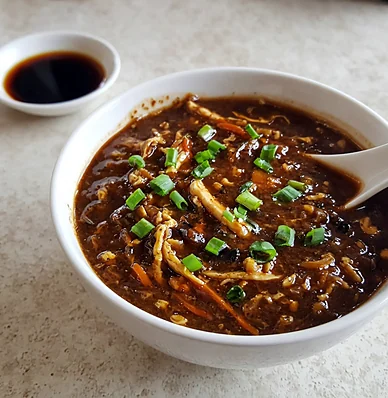 A bowl of hot and sour soup with shredded vegetables and spring onion
