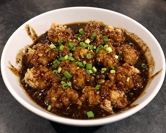 Chicken Manchurian in a dark garlic soy gravy with spring onion, in a white bowl