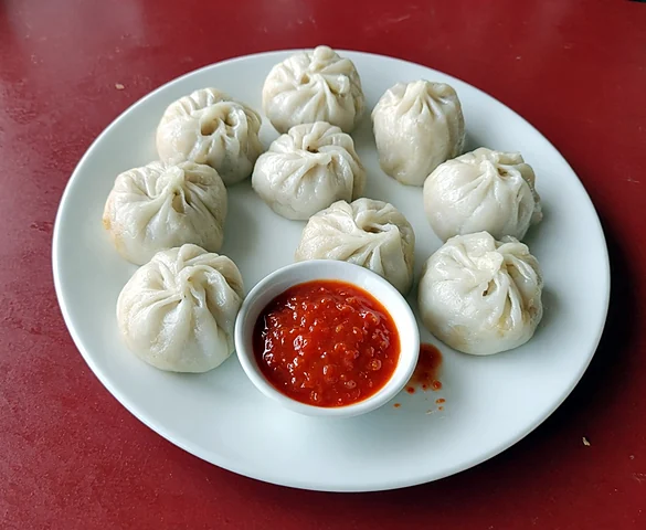 Eight steamed chicken momos around a bowl of red chilli chutney